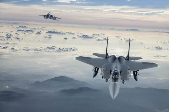 Two fighter jets in the air above the clouds.